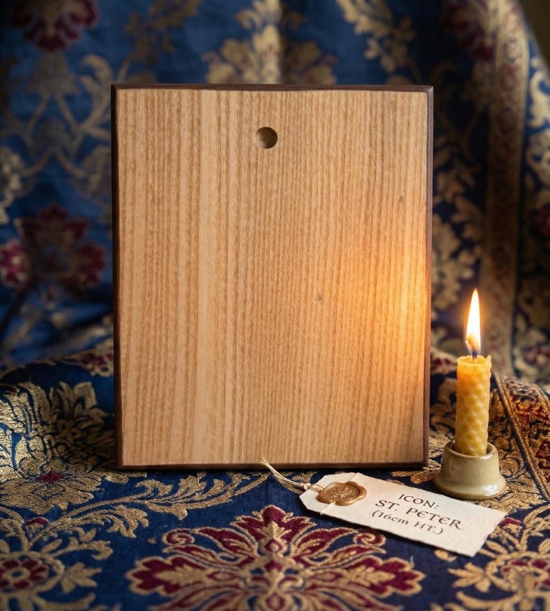 May include: Wooden icon of St. Peter, with a light brown wood grain. The icon has a dark brown border and a small hole at the top. A lit beeswax candle sits to the right. A tag reads "ICON: ST. PETER (16cm HT.)".