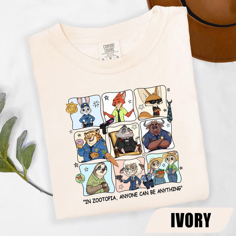 May include: Ivory-colored t-shirt featuring a grid of cartoon characters from Zootopia. Each character is in a different profession. The text "IN ZOOTOPIA, ANYONE CAN BE ANYTHING" is printed at the bottom. The shirt is labeled "IVORY".