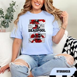 以下が含まれることがあります： デッドプールのグラフィックが特徴のライトブルーのTシャツ。デザインには、デッドプールのイラストが描かれた3つのパネルと、黒で「DEADPOOL EST. 1991」の文字が含まれています。このTシャツは、クルーネックで半袖です。