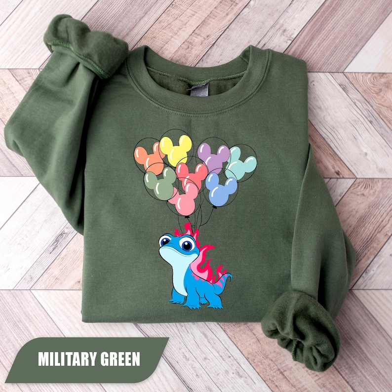 May include: Military green sweatshirt featuring a cartoon blue lizard with pink flames and colorful Mickey Mouse balloon graphics. The text "MILITARY GREEN" is displayed at the bottom of the image.