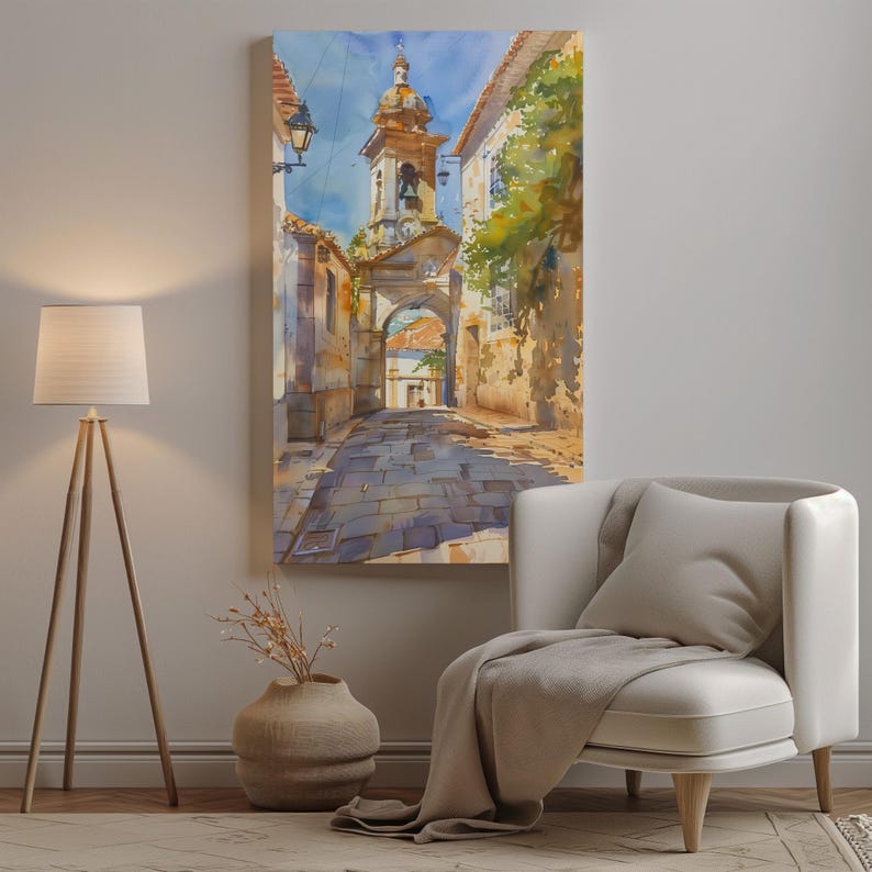 Puede incluir: Pintura a la acuarela de una escena de calle europea. La obra representa una calle adoquinada que conduce a una puerta arqueada y un campanario. Los edificios con fachadas envejecidas bordean la calle, y el cielo es azul claro.