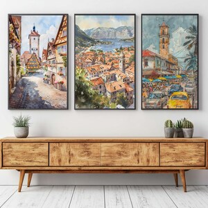 May include: Set of three framed watercolor prints depicting European cityscapes. The artwork features detailed renderings of streets, buildings, and landscapes, with a focus on architectural and natural elements. The color palette includes warm tones and vibrant blues.