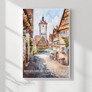 May include: Watercolor print of Rothenburg ob der Tauber, Germany. The artwork depicts a cobblestone street lined with colorful buildings, a clock tower, and vibrant flowers. The image has a soft, painterly quality, capturing the charm of the historic town.