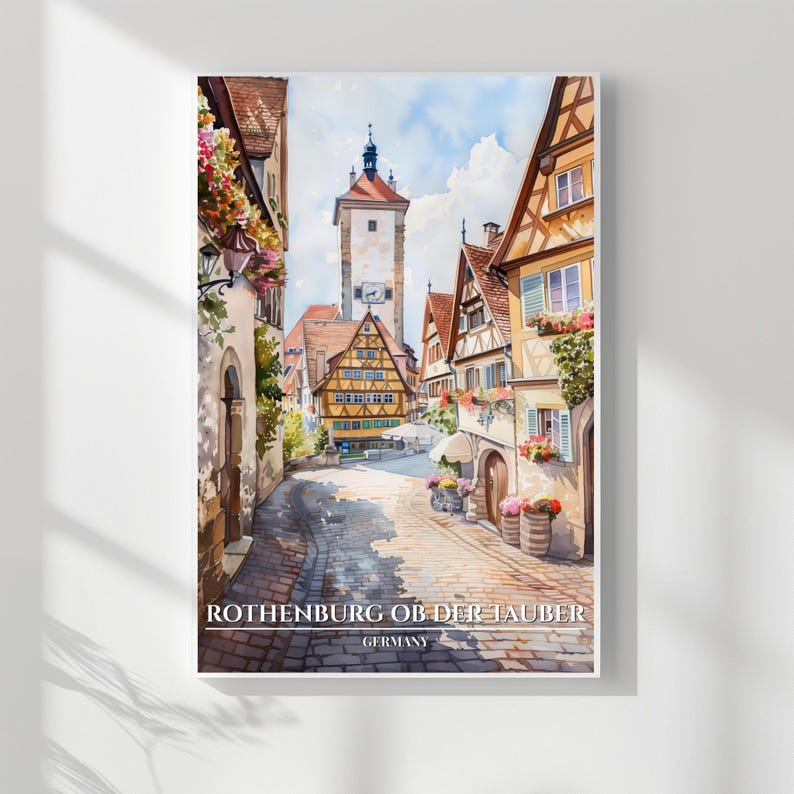 May include: Watercolor print of Rothenburg ob der Tauber, Germany. The artwork depicts a cobblestone street lined with colorful buildings, a clock tower, and vibrant flowers. The image has a soft, painterly quality, capturing the charm of the historic town.