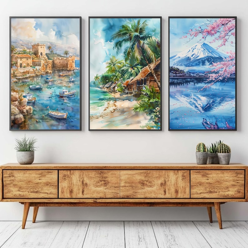 May include: Three framed watercolor paintings depicting coastal scenes. One shows a harbor with boats and buildings, another a tropical beach with palm trees, and the third a mountain landscape with cherry blossoms. The paintings are displayed above a wooden cabinet.