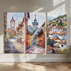 May include: Triptych of watercolor prints depicting European cityscapes. The prints feature cobblestone streets, colorful buildings, and the text "HENBURG OB DER TAU GERMANY", "SIGHISOARA ROMANIA", and "BERAT ALBANIA".