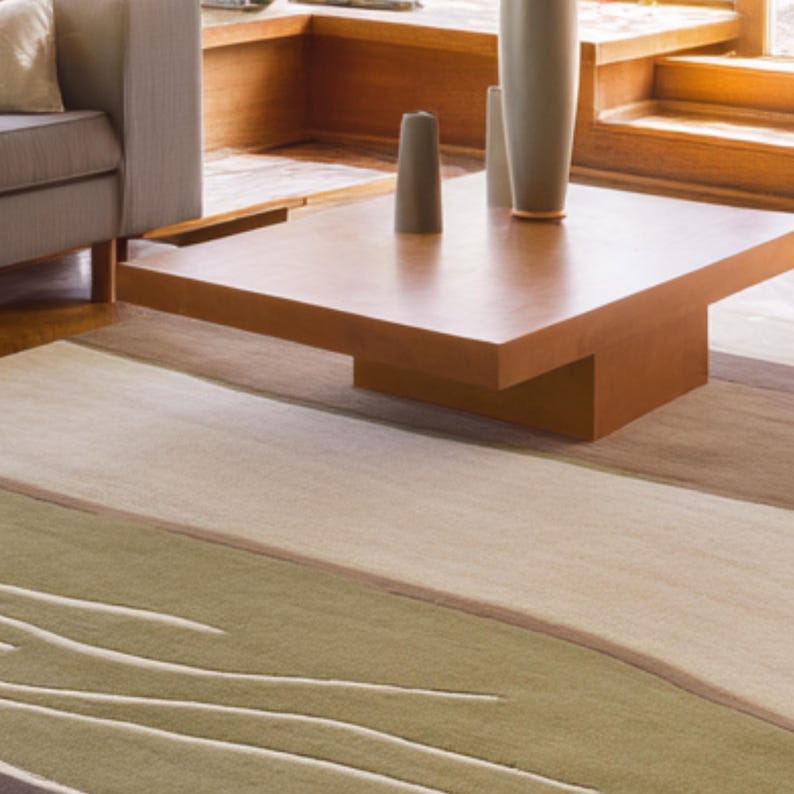 May include: A modern living room scene featuring a square, brown coffee table with a minimalist design. The table is set on a patterned rug with shades of green, beige, and brown. Decorative vases in muted tones sit on the table, complementing the room's neutral color palette.