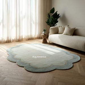 May include: A cloud-shaped area rug with a light blue and cream color scheme. The rug has a scalloped edge with a darker blue border. The rug is placed in a living room setting with a sofa, curtains, and a wooden side table.