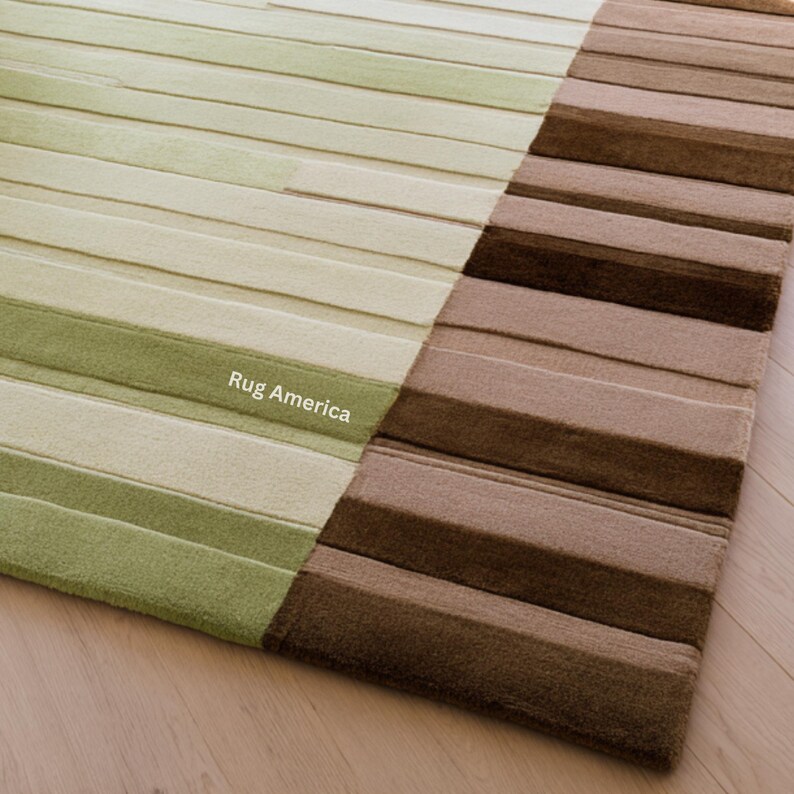 Pu&ograve; includere: Un tappeto rettangolare con un design a righe. Il tappeto &egrave; diviso in due sezioni, una con sfumature di verde e l'altra con sfumature di marrone. Il testo "Rug America" &egrave; visibile sulla sezione verde.