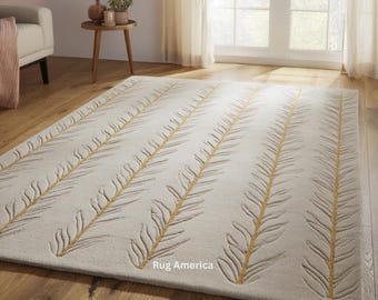 May include: A rectangular, off-white rug with a repeating pattern of stylized, yellow and gray leaf-like designs. The rug is placed on a hardwood floor in a well-lit room. The text "Rug America" is visible on the rug.