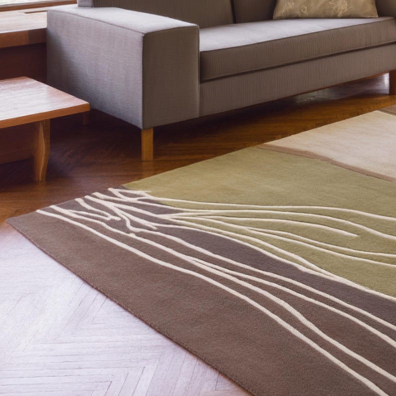 May include: A rectangular area rug with a brown, green, and beige color scheme. The rug features a design of white, curved lines against a brown background, with a green and beige section. The rug is placed on a hardwood floor.