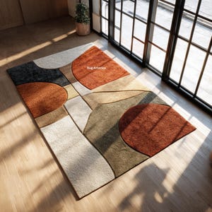 Op de afbeelding: Een modern vloerkleed met een abstract geometrisch ontwerp. Het vloerkleed heeft een combinatie van roest-, beige-, grijs- en zwarttinten. De tekst "Rug America" is zichtbaar op het vloerkleed.