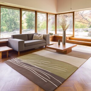 May include: A modern living room with a gray sofa, wooden coffee table, and a large area rug. The rug features a brown, green, and beige color scheme with white linear designs. Large windows offer a view of the outdoors.