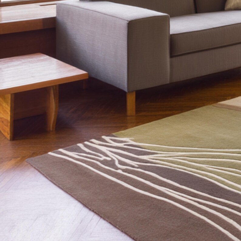 May include: A modern living room scene featuring a brown and green area rug with a white abstract design. A gray sofa and wooden side table are also visible. The rug's design resembles tree branches.