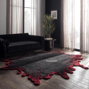 Può includere: Un grande tappeto astratto con un centro grigio scuro e un bordo rosso vibrante e irregolare. Il design del tappeto ricorda uno schizzo o una macchia, aggiungendo un tocco moderno alla stanza. Il testo "Rug America" è visibile sul tappeto.