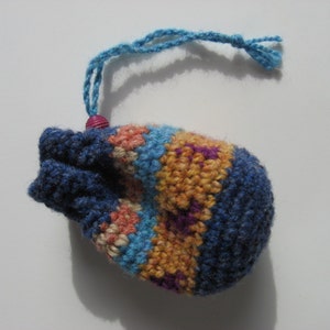 May include: A small crocheted drawstring bag with a blue, orange, pink, and purple striped pattern. The bag has a blue cord with a pink bead.