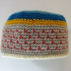 May include: A handmade crochet beanie in a color block design. The hat features a light gray base with red accents, a yellow stripe, and a blue stripe at the top. The brim is a cream color.