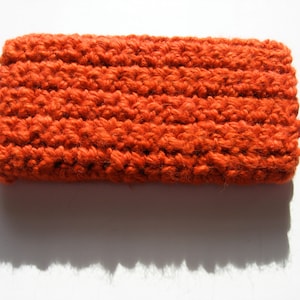 May include: A close-up of a knitted headband in a bright orange color. The headband is made of a soft, textured yarn and has a simple, classic design.