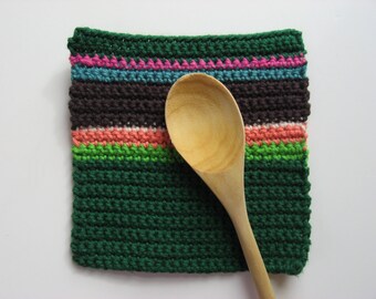May include: A green crocheted pot holder with colorful stripes, featuring a wooden spoon resting on top.