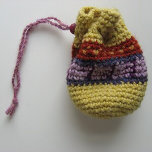 May include: A small crocheted drawstring bag with a purple and yellow striped pattern. The bag has a purple drawstring.
