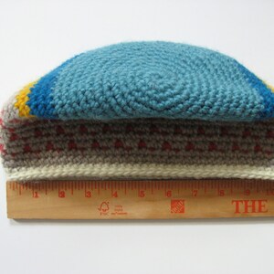 May include: A handmade crochet hat with a blue top, a yellow and blue stripe, and a gray and red patterned band. The hat measures approximately 11 inches in length.