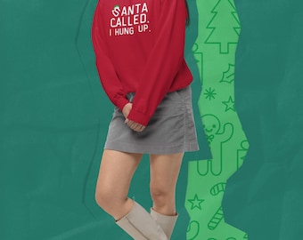 May include: A red long-sleeve sweatshirt with the text "SANTA CALLED. I HUNG UP." is worn with a gray skirt and light-colored boots. The background is green with Christmas-themed graphics.