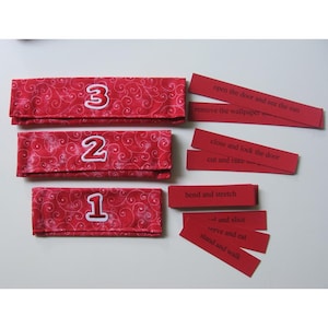 Peut inclure: Trois pochettes en tissu rouge avec des chiffres brodés blancs 1, 2 et 3. Chaque pochette a une bande de papier rouge avec une phrase d'action différente : "ouvrir la porte et voir le soleil", "fermer et verrouiller la porte", "plier et étirer". Il y a aussi quatre autres bandes de papier rouge avec les phrases : "enlever le papier peint", "couper et ratisser", "-- et trancher", "servir et manger", et "se tenir debout et marcher".