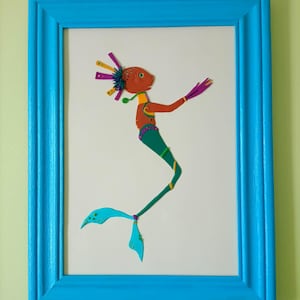 May include: A framed artwork depicting a colourful, whimsical mermaid-like figure. The art piece has an orange head, green tail, and purple accents. The frame is a bright blue, adding a vibrant touch to the artwork.