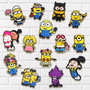 May include: A collection of colorful Minion-themed character charms. The charms feature various designs, including characters dressed as a maid, superhero, and Batman. The background is a white brick wall.