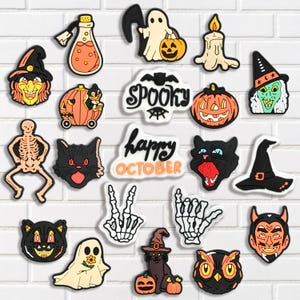 May include: A collection of Halloween-themed charms in various shapes, including pumpkins, cats, ghosts, and witch hats. The charms are in black, orange, and white, with the words "Spooky" and "Happy October".