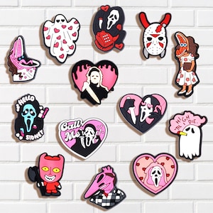 May include: A collection of colorful shoe charms featuring various horror movie characters and themes. Designs include a ghost with hearts, a heart-shaped design with a knife, and characters from Scream, Beetlejuice, and Halloween.