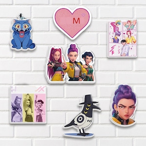 May include: A collection of colorful stickers featuring cartoon characters and designs. Includes a blue cat, a pink heart with the letter "M", a crow, and several images of stylized people. The stickers are arranged on a white brick wall.