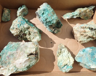 May include: A collection of eight rough, green and white mineral specimens in a cardboard box. The minerals have a variety of shapes and sizes.