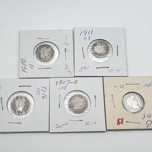 May include: Five silver coins in protective holders are displayed against a white background. The coins are dated 1907-O, 1910, 1911, and 1916. Each coin features a profile of a woman and the words "United States of America".