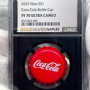 May include: A red Coca-Cola bottle cap with the Coca-Cola logo in white, encased in a clear protective holder. The holder includes a label with text: "2023 Niue S$1 Coca-Cola Bottle Cap PF 70 ULTRA CAMEO".