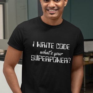May include: Black t-shirt with the text "I WRITE CODE what's your SUPERPOWER?" in white. The shirt is a crew neck and is being worn by a person. The person is wearing blue jeans.