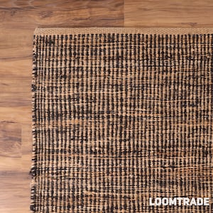 May include: A rectangular area rug featuring a woven texture with alternating vertical stripes of dark brown and natural tan fibers. The rug has a thick, braided border along the top edge and the text LOOMTRADE is printed in white in the bottom corner.
