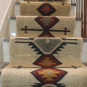 Puede incluir: Alfombras de pasillo para escaleras con patrones geométricos en beige, rojo, negro y amarillo. Las alfombras están instaladas en una escalera con escalones blancos. El texto "Loom Trade" es visible en una de las alfombras.