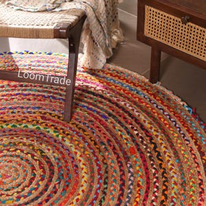 May include: A round jute rug with a braided design in a spiral pattern. The rug features a mix of colors including red, blue, yellow, and green. The text "LoomTrade" is visible on the side of a wooden chair.