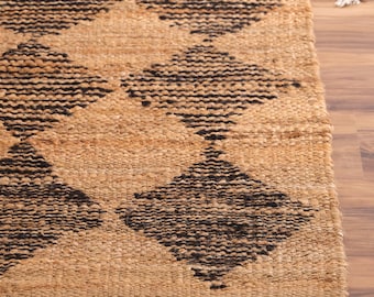 May include: A rectangular woven rug featuring a natural tan fiber base with a repeating dark brown diamond pattern. The word LOOMTRADE is printed in white text near the top edge of the rug, which has a thick, textured, braided construction.