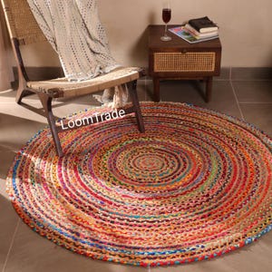 May include: A round, multi-colored jute rug with a spiral design. The rug features a vibrant mix of red, orange, yellow, green, and blue hues. The rug is placed on a tiled floor near a wooden chair and side table.
