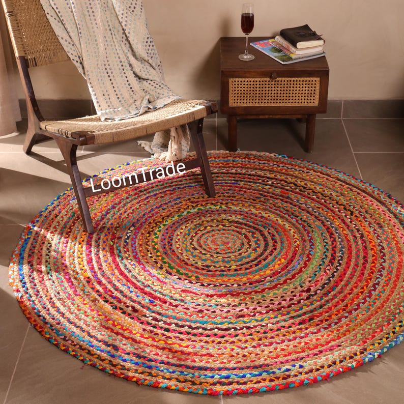 May include: A round, multi-colored jute rug with a spiral design. The rug features a vibrant mix of red, orange, yellow, green, and blue hues. The rug is placed on a tiled floor near a wooden chair and side table.