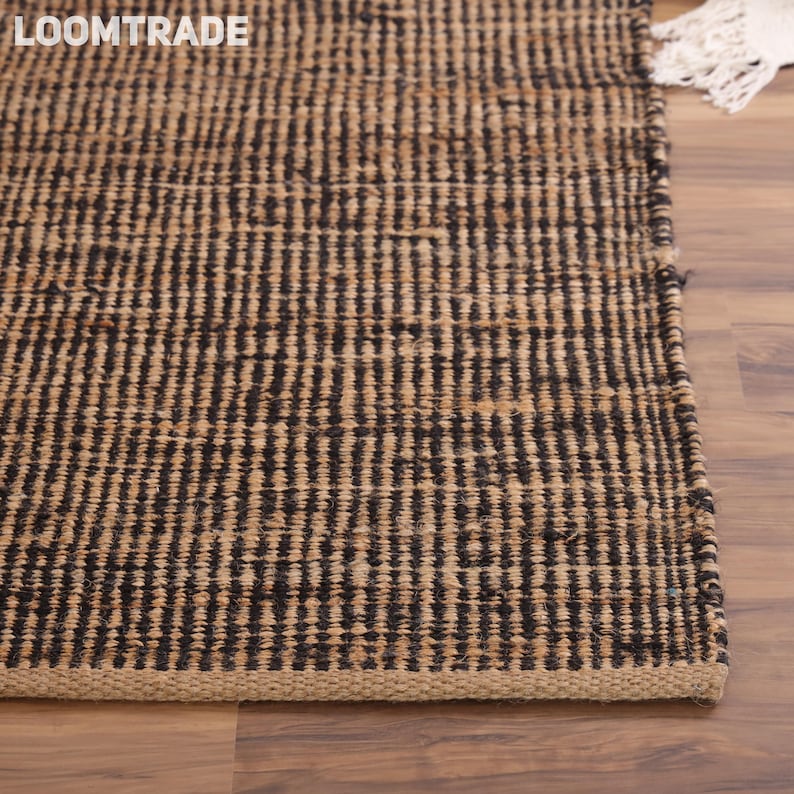 May include: A rectangular area rug featuring a woven pattern of alternating vertical stripes in dark brown and natural tan fibers. The rug has a thick, textured weave and a finished edge, with the text LOOMTRADE visible in the upper left corner.
