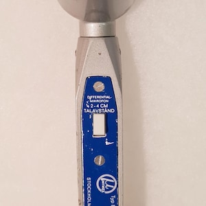Könnte beinhalten: Vintage silbernes Mikrofon mit schwarzem Mesh-Kopf. Das Mikrofon hat ein blaues Etikett mit weißem Text, der "DIFFERENTIAL- MIKROFON 2-4 CM TALAVSTÅND STOCKHOLM - SWEDEN" lautet. Ein rotes Spiralkabel erstreckt sich von der Basis.