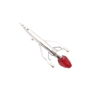 May include: A silver rocket ship figurine with a red crystal at the end. The rocket ship is pointed upwards and has a sleek, modern design.