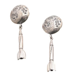 May include: Silver earrings with a textured moon charm and a rocket pendant.