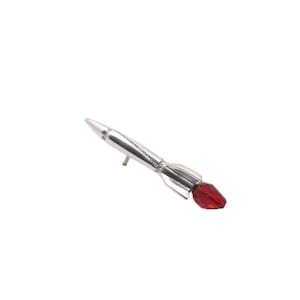 May include: A silver rocket-shaped pin with a red crystal at the tip.