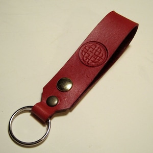 May include: A red leather keyring with a Celtic knot design and two gold-toned metal rivets. The keyring has a silver metal ring.
