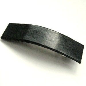 Könnte beinhalten: Eine schwarze Haarklammer aus Leder mit glatter, glänzender Oberfläche.