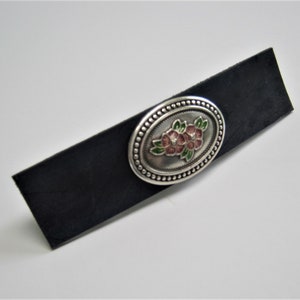 May include: A silver oval-shaped buckle with a floral design. The buckle has a beaded border and features pink and green enamel flowers.